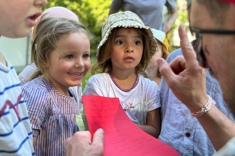 Children sitting outdoors with a person holding a red piece of paper